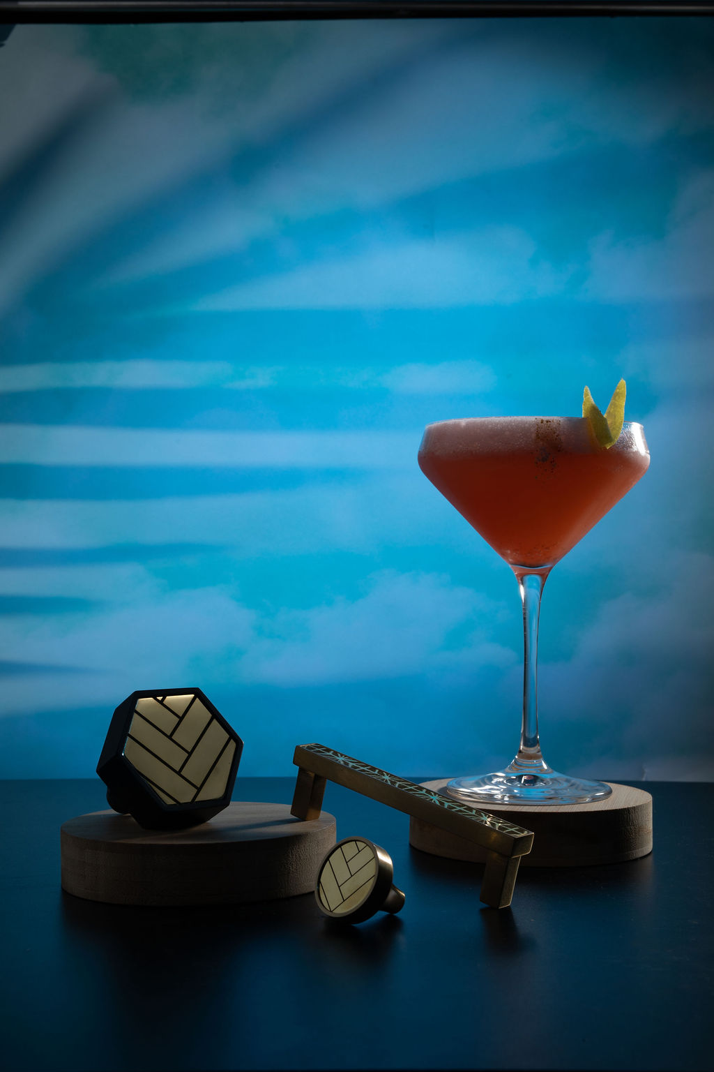 Coral coupe cocktail with geometric bar accessories and blue sky backdrop