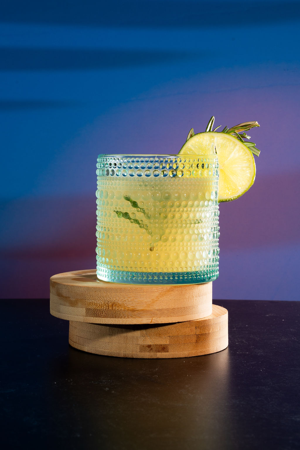 Signature lime cocktail on wooden coasters with blue gradient background