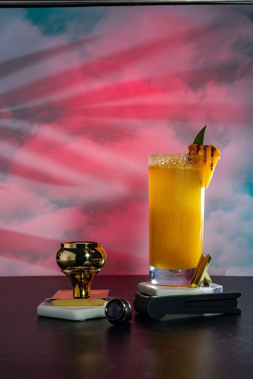 Tropical pineapple cocktail with grilled garnish and pink sky backdrop